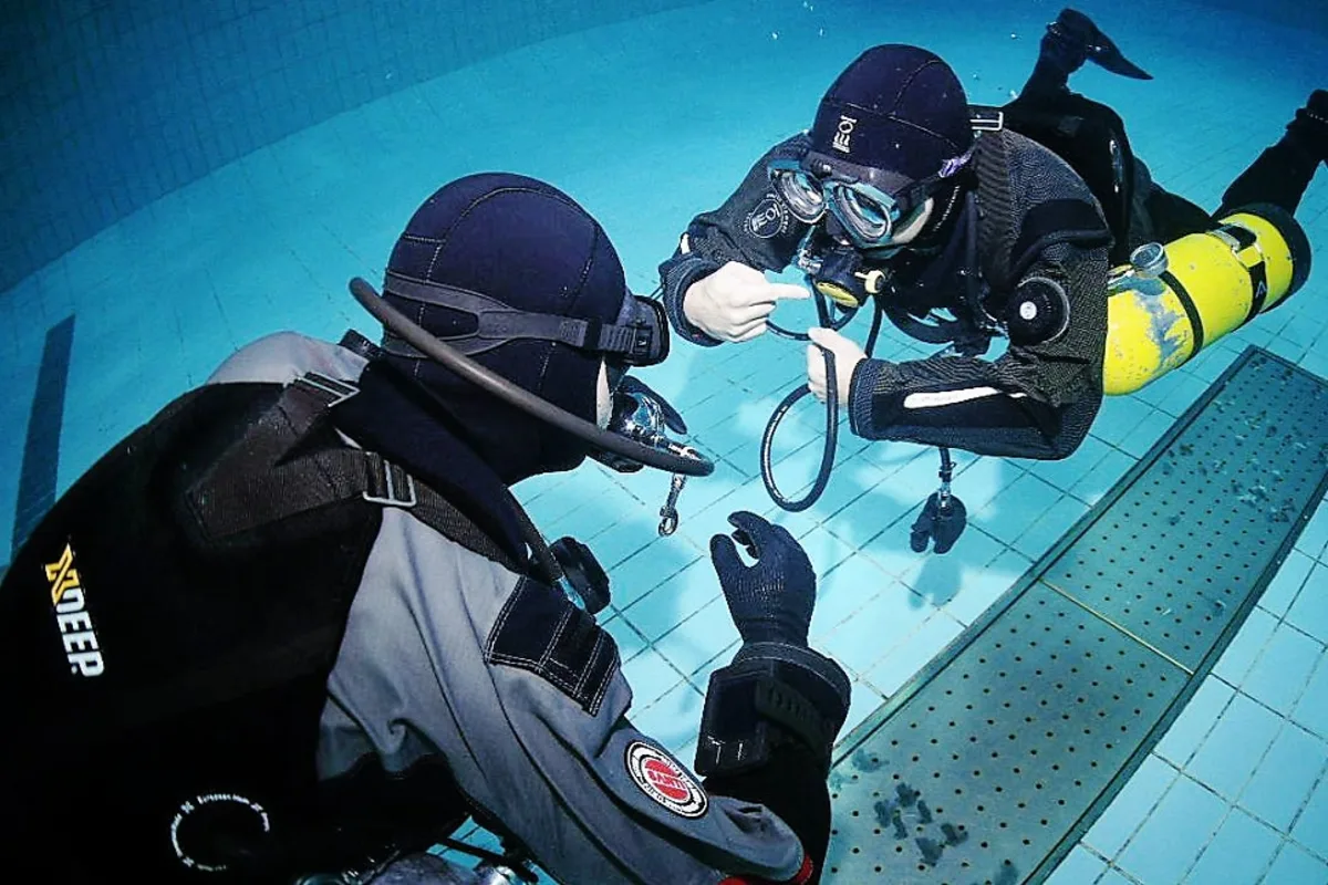 Instructor adjusting a student's equipment underwater during a diver essentials course gear fitting session
