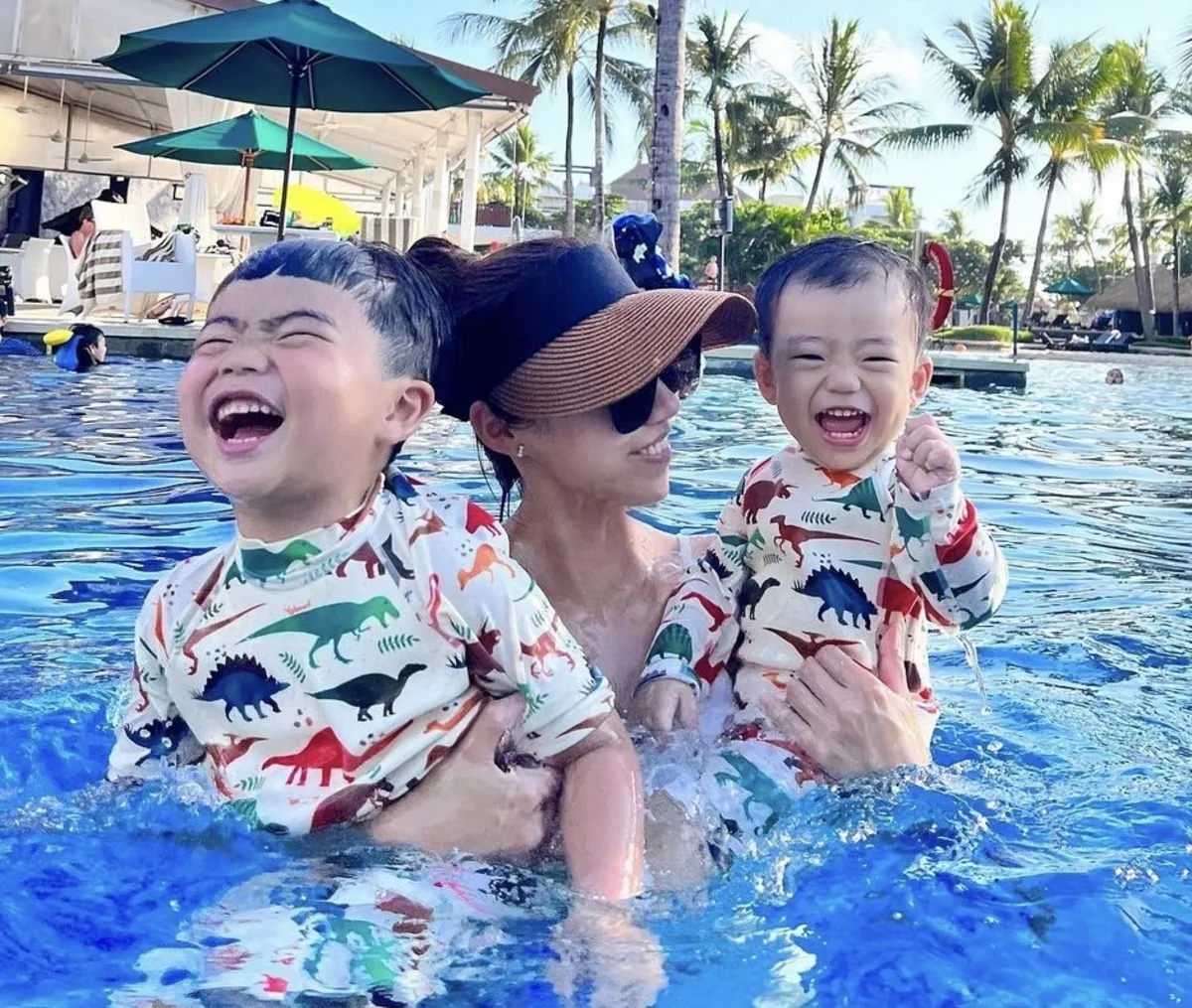 Scuba diving mom laughing in a pool with her two young children, both learning to love the water