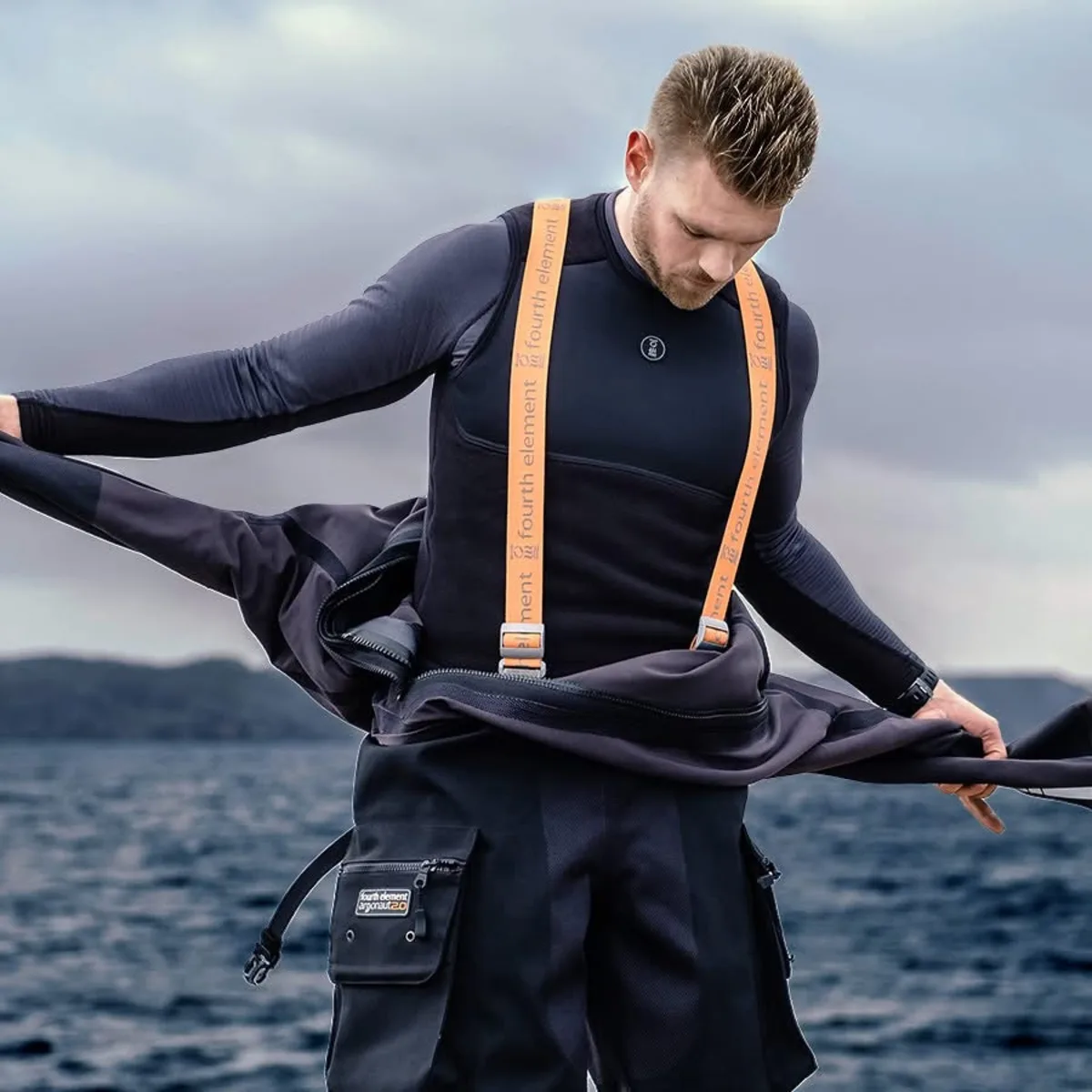 Diver pulling a drysuit up over a base layer and undersuit, the layering step of drysuit care
