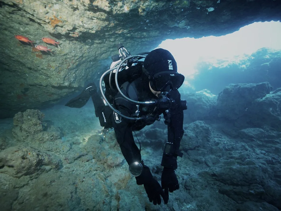 Scuba diver hovering at the mouth of an Okinawa cavern with sunlight behind, first overseas dive trip from Korea