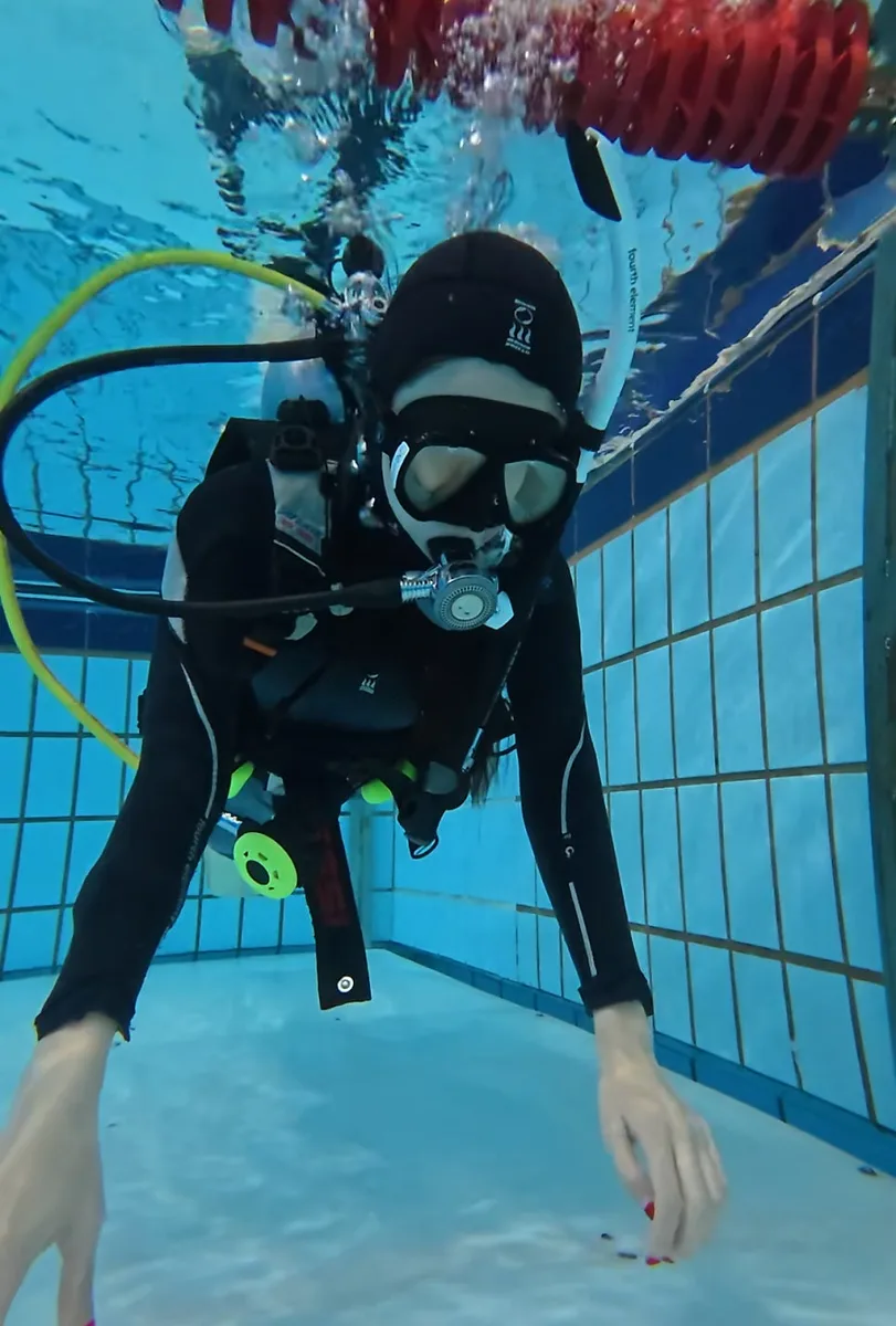 A scuba student descending slowly in a training pool, where equalisation technique for scuba ear pain is first practised