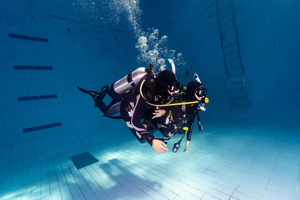 A diver holding trim horizontally in a training pool while working a camera, the core skill of an underwater photography course in Seoul